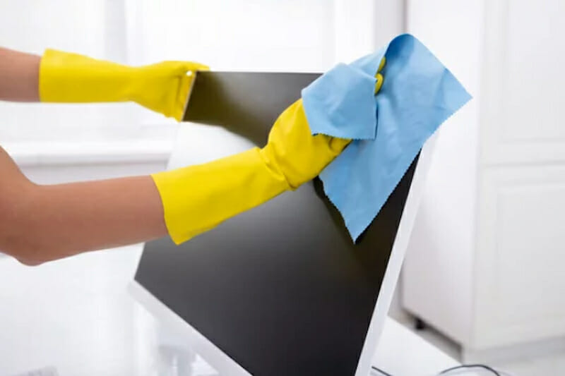 a peron wearing yellow rubber gloves cleaning the white monitor